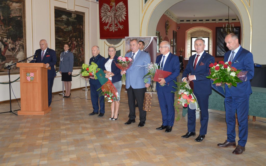 Grupa samorządowców z powiatu brzeskiego z kwiatami i prezentami dla komendanta policji